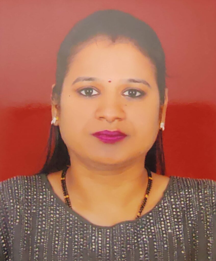 Portrait of a woman facing the camera against a red background, wearing a small red bindi, earrings, and purple lipstick with a beaded necklace.